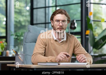 Porträt eines kreativen Büromitarbeiters, der mit einem Computer an einem Tisch sitzt und ernsthaft in die Kamera schaut. Stockfoto