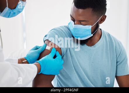 afroamerikaner Patient schaut auf den Arzt beim Pflasterlegen. Patient im Gespräch mit einem Arzt. Patient trägt eine Maske zum Schutz vor Kokosnuss Stockfoto
