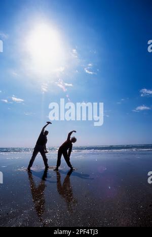 Ein Seniorenpaar, das an einem Sommertag am Strand Kalisthenics macht Stockfoto