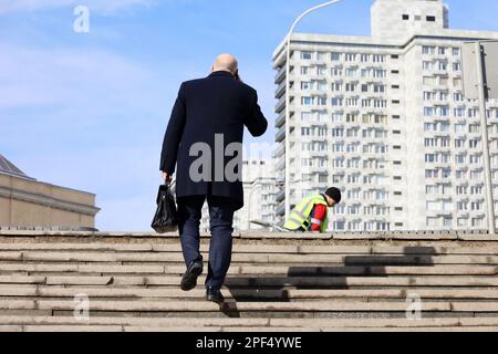 Mann in einem Geschäftsanzug und Mantel mit Lederaktentasche in der Hand, klettert Steintreppen in der Stadt und spricht mit dem Handy. Konzept von Karriere, Erfolg Stockfoto