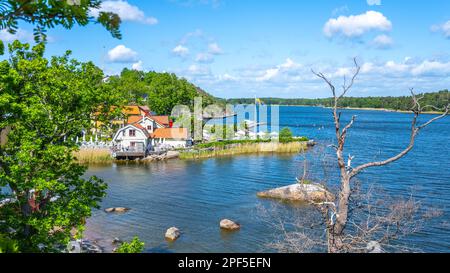 Sonniger Tag in einer kleinen Dorfbucht auf der Insel Vaxholm. An der Küste befindet sich das Hembygdsgard Museum und eine ruhige Terrasse mit Sitzbereichen für Gäste. Stockholmer Archipel, Schweden Stockfoto