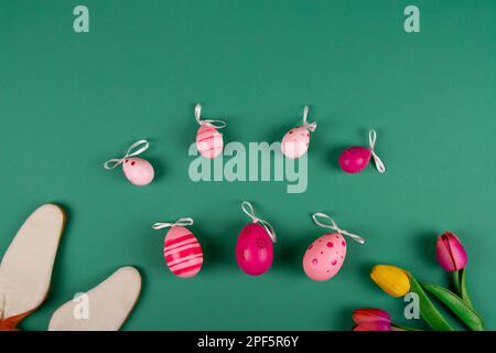Blumen, Ostereier und weiche Hasenohren auf dunkelgrünem Hintergrund Stockfoto