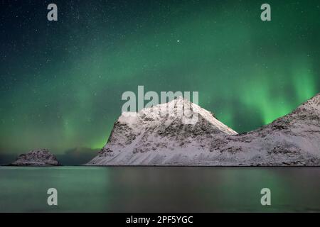 Helle aurora mit Reflexion im Wasser und Sternenhimmel mit Milchstraße über einer Bergkette, teilweise im Mondlicht beleuchtet - Lage: Norwegen, Lo Stockfoto