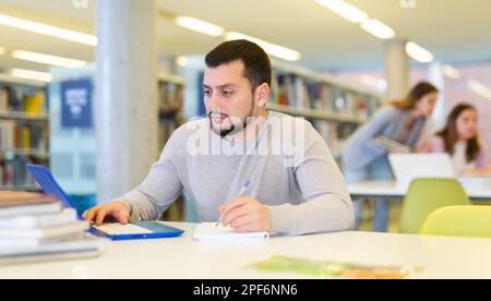 Fokussierte Schüler studieren in der Bibliothek auf einem Laptop Stockfoto