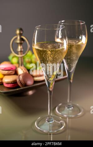 Gläser Sekt, Sekt, Brut oder Cava mit Blasen und süßem Dessert, bunte Makronen-Kekse im Hintergrund Stockfoto