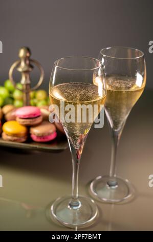 Gläser Sekt, Sekt, Brut oder Cava mit Blasen und süßem Dessert, bunte Makronen-Kekse im Hintergrund Stockfoto