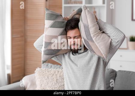 Junger Mann mit Kissen, der zu Hause unter lautem Lärm leidet Stockfoto