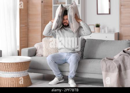 Junger Mann mit Kissen, der zu Hause unter lautem Lärm leidet Stockfoto