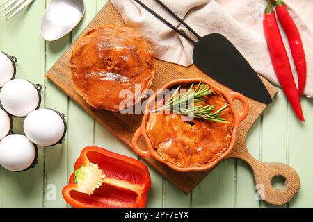 Zusammensetzung mit köstlichen Fleischpasteten und Zutaten auf einem grünen Holztisch Stockfoto