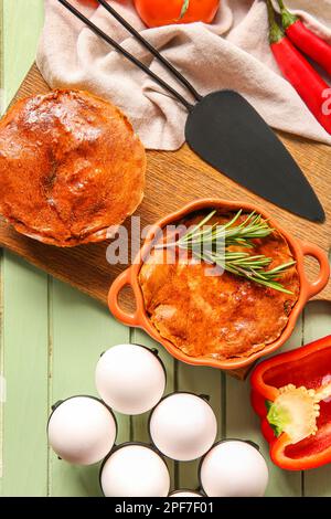 Zusammensetzung mit köstlichen Fleischpasteten und Zutaten auf einem grünen Holztisch Stockfoto