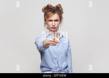 Du bist an meinem Unglück schuldig. Unzufriedene blonde Frau, die jemandem die Schuld gibt, direkt auf die Kamera zeigt, ernstes Gesicht macht, blaues Hemd trägt. Studioaufnahmen im Innenbereich isoliert auf grauem Hintergrund. Stockfoto