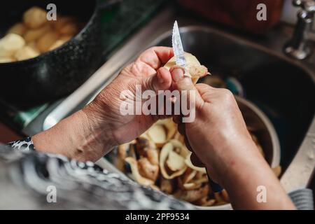 Nahaufnahme der Hände einer lateinamerikanischen Frau, die Kartoffeln in ihrem Spülbecken schält Stockfoto