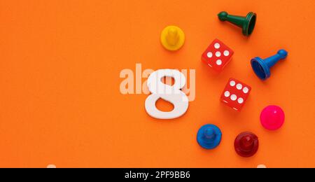 Nummer acht in Weiß mit Steinen und Spielwürfeln - Hintergrund aus orangefarbenem eva-Gummi Stockfoto