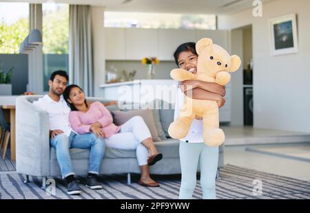 Sie lässt den Bären nie gehen. Ein kleines Mädchen, das ihren Teddybär hält, während ihre Eltern zuschauen. Stockfoto