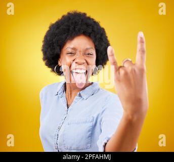 Rock Hand, Metall und schwarze Frau Porträt im Studio mit ausgezogener Zunge für Punk-Musik. Glück, Freiheit und kühle junge Frau mit isoliertem Gelb Stockfoto