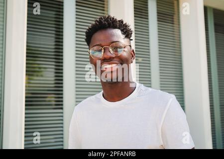 Porträt eines jungen afroamerikanischen Teenagers, der lächelt und draußen in die Kamera schaut. Vorderansicht eines glücklichen und fröhlichen Mannes mit Brille und weißen perfekten Zähnen. Lyfestyle-Konzept. Hochwertiges Foto Stockfoto
