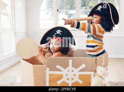 Pirat, Box und Teleskop mit Kindern im Wohnzimmer für verspielte, kreative und fantasievolle Momente. Fantasie, Entspannung und Party mit Kindern, die in einem Pappboot segeln Stockfoto