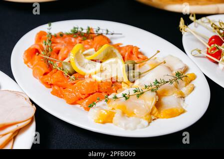 Geschnittene Filets von fetten Fischen. Geräucherter Lachs mit Zitronenscheiben und Heilbuttfilets mit großen Kapern. Nützliches Produkt reich an Omega-3. Stockfoto