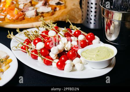 Leckere Vorspeise mit Mozzarella und Kirschtomaten auf Spießen und Dippsoße auf dem Tisch. Ein großer Haufen Caprese Canapes. Stockfoto