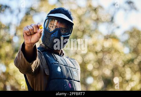 Mann, Paintball und Hände halten den Ball auf dem Schlachtfeld für den Krieg, erschossen oder spielen in der Natur. Männlicher Paintballer oder Soldat zeigt oder kneift Stockfoto