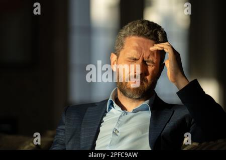 Gestresster Geschäftsmann mit Kopfschmerzen im Home Office. Ein müder Geschäftsmann macht Überstunden und hat Kopfschmerzen. Das Porträt des Senioren leidet an Kopfschmerzen Stockfoto