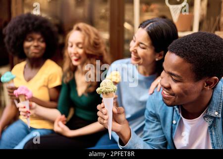 Ein afrikanischer Mann, der draußen mit Freunden ein Eis isst Stockfoto