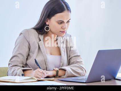 Sie plant immer etwas großes. Eine junge Geschäftsfrau, die Notizen schreibt, während sie in einem Büro an einem Laptop arbeitet. Stockfoto