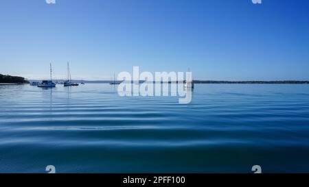 Blick über ruhige Gewässer, vor der Küste von Coochiemudlo Island vorbei an Booten nach Macleay und Stradbroke Inseln am Horizont Stockfoto