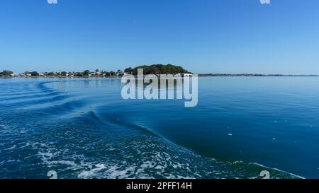 Blick von der Fähre auf dem Weg zur Insel Coochiemudlo. Blicken Sie zurück über das ruhige Wasser und wachen Sie von der Fähre nach Victoria Point in der Ferne auf. Stockfoto