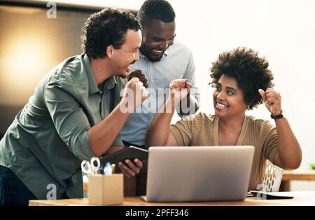 Wir haben es geschafft. Eine junge Gruppe von Geschäftsleuten, die gemeinsam eine Leistung feiern, während sie ein Notebook verwenden. Stockfoto
