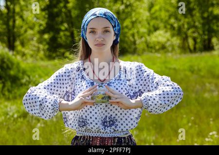 Frau mit transparenter Teekanne und Kräutertee. Sammelt frische grüne Kräuter, ernten und machen gesunden Tee. Verschwommenes Bild, selektiver Fokus Stockfoto