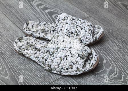 Weiße handgestrickte Hausschuhe stehen auf einem grauen Holzboden Stockfoto