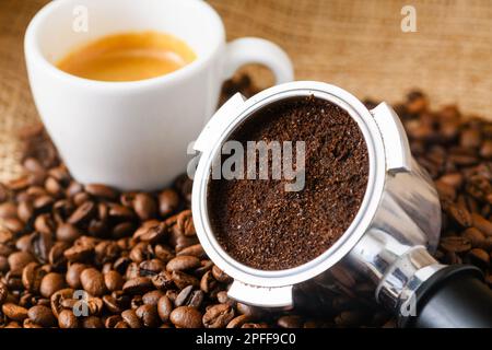 Verbrauchter oder gebrauchter Kaffeesatz mit Portafilter und einer Tasse frisch gebrühtem Kaffee im Hintergrund Stockfoto