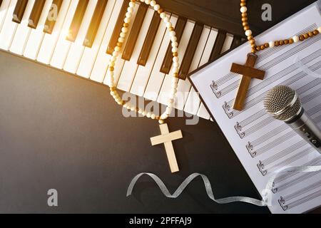 Religiöse Musik mit Klavier und Mikrofon auf Notenblättern auf einem schwarzen Tisch mit Kreuzen und goldenem Glitzer. Draufsicht. Stockfoto