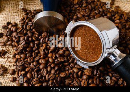 Makro-feines Mahlkaffee für Espresso im Metallhalter für Möbelautomaten mit Stampfer, Halter und Bohnen, natürlicher Hintergrund Stockfoto
