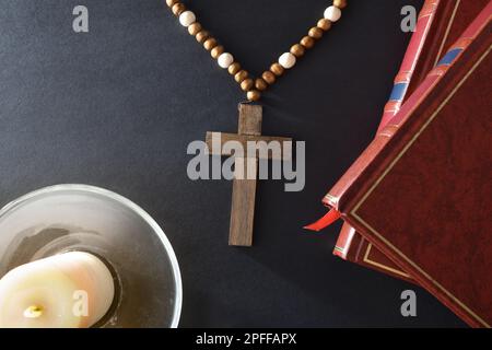 Schwarzer Nachttisch mit religiösen Elementen zum Beten mit einer christlichen Kreuzbibel und einer Kerze auf einem Glasteller. Draufsicht. Stockfoto