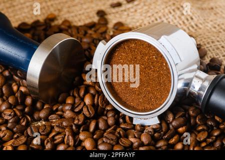 Gestampfter Puck Kaffeepulver in einem Korb aus Portafilter und Kaffeebohnen, die auf den Hintergrund geschüttet wurden Stockfoto