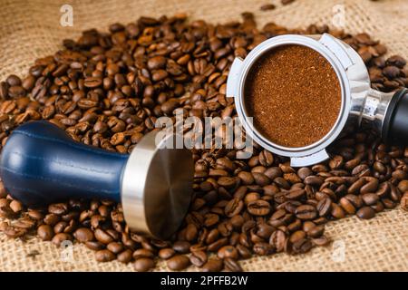 Gestampfter Puck Kaffeepulver in einem Korb aus Portafilter und Kaffeebohnen, die auf den Hintergrund geschüttet wurden Stockfoto