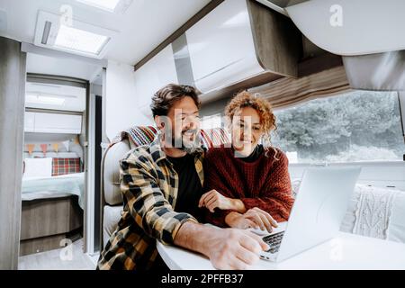 Glückliche Reise Paar Lifestyle Lächeln und verwenden Laptop zusammen in einem modernen Wohnmobil in Vanlife Offgrid alternative Büroarbeitsplätze. Abenteuerleben Stockfoto