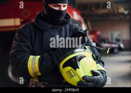 Porträt eines Feuerwehrmanns in Schutzuniform, das die süße kleine schwarze Katze hält Stockfoto