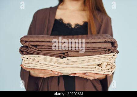 Nahaufnahme einer jungen Frau, die mit Bettwäsche in den Händen an der Wand steht Stockfoto