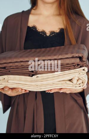 Nahaufnahme einer jungen Frau, die mit Bettwäsche in den Händen an der Wand steht Stockfoto