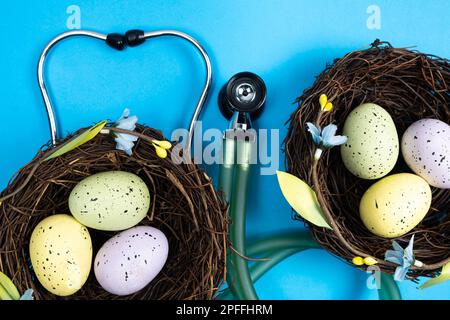 Ostermedizin. Zwei Nester mit bemalten Eiern und ein Stethoskop auf blauem Hintergrund. Stockfoto