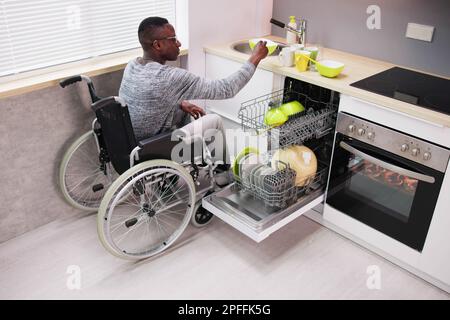 Junger Mann, Der Auf Dem Rollstuhl Sitzt Und Teller In Der Spülmaschine Arrangiert Stockfoto