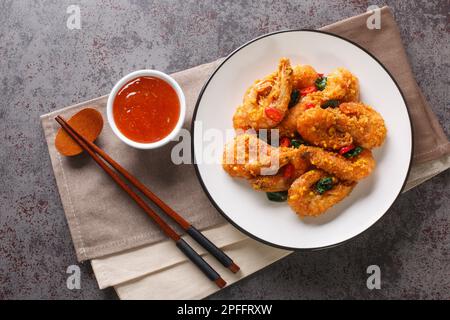 Knusprige, köstliche gebratene Shrimps mit gesalzenem Eigelb, Curryblättern und Chili-Paprika, serviert mit Chilisauce aus nächster Nähe auf einem Teller auf dem Tisch. Horizont Stockfoto