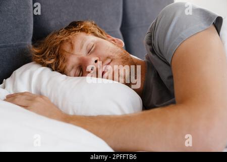 Porträt eines jungen, attraktiven, schlafenden Rothaarigen im grauen T-Shirt zu Hause im Bett Stockfoto