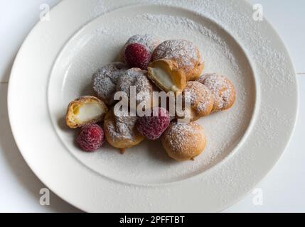 Köstliche Profiteroles, Konzept von hausgemachtem Gebäck, Präsentation von Profiteroles dekoriert mit Erdbeeren auf einem weißen Teller, Draufsicht. Stockfoto