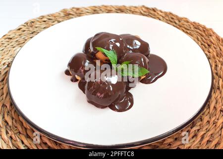 Köstliche Profiteroles mit Schokolade, Schokoladen-Profiteroles auf einem weißen Teller, Nahaufnahme. Stockfoto