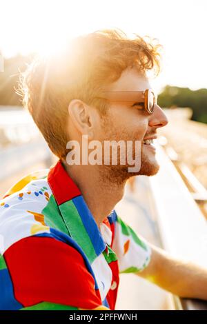 Profilbild eines gutaussehenden, lächelnden Mannes mit Sonnenbrille und farbenfrohem Hemd, der in der Sonne sitzt Stockfoto