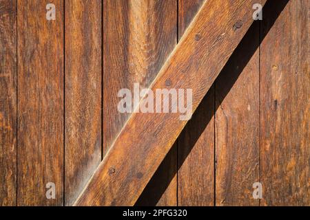 Detail der alten unlackierten Holztür mit vertikalen Leisten und einer diagonalen Leiste in braunen Farbtönen. Stockfoto
